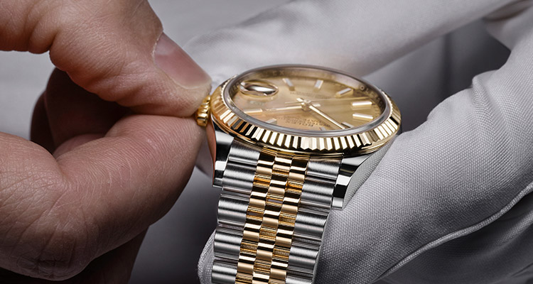 Eine Rolex Uhr wird von einem Mitarbeiter vom Service mit weißen Handschuhen durch Drehen der Krone richtig eingestellt 