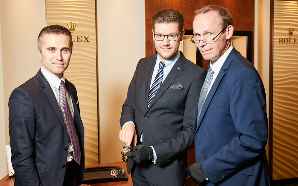 Geschäftsleiter André Ustinov von Juwelier Mahlberg steht neben Verkaufsberater Jan-Sebastian Saretzki, der eine Rolex Uhr hält und Uhrmachermeister Norbert Ludwig.